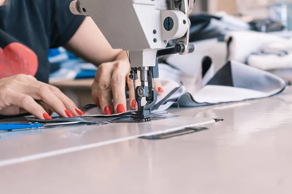 The seamstress sews on an old sewing machine, threads the fabric. Women's hands