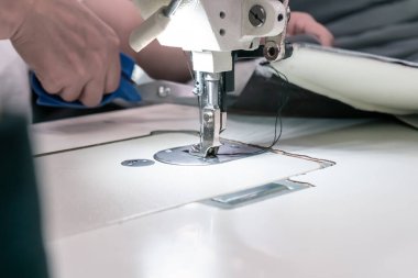 A seamstress cuts fabric while working at a sewing machine in the workshop. Women's hands