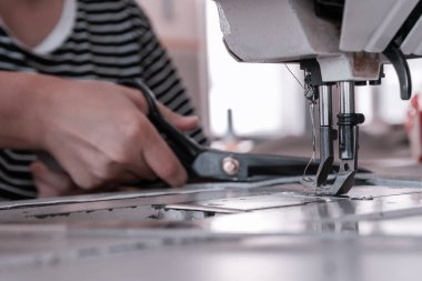 A seamstress cuts fabric while working at a sewing machine in the workshop. Women's hands