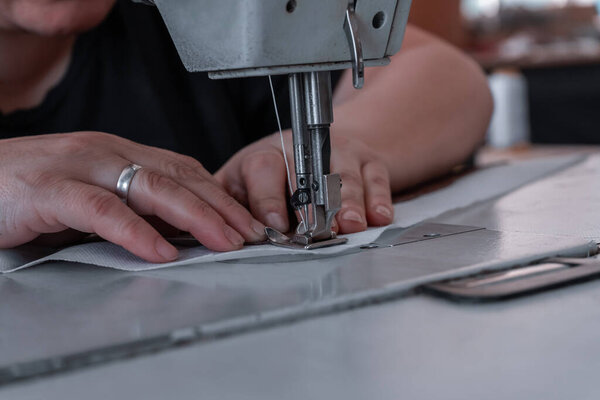 The seamstress sews at the sewing machine, threads the fabric. Women's hands