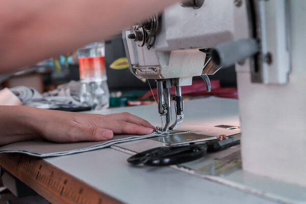 The seamstress sews at the sewing machine, threads the fabric. Women's hands
