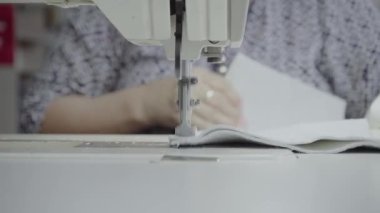 Atölyedeki bir terzi dikiş makinesine beyaz iplikçikli, hakiki deriden yapılmış bir ürün dikiyor.