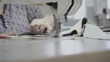 Atölyedeki bir terzi dikiş makinesine beyaz iplikçikli, hakiki deriden yapılmış bir ürün dikiyor.