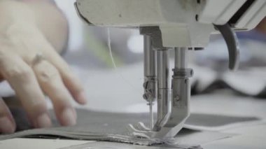 Atölyedeki bir terzi dikiş makinesine beyaz iplikçikli, hakiki deriden yapılmış bir ürün dikiyor.