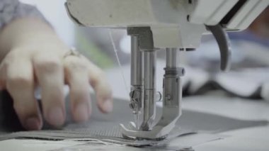 Atölyedeki bir terzi dikiş makinesine beyaz iplikçikli, hakiki deriden yapılmış bir ürün dikiyor.