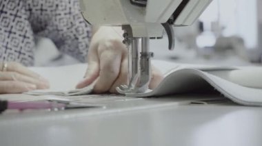 Atölyedeki bir terzi dikiş makinesine beyaz iplikçikli, hakiki deriden yapılmış bir ürün dikiyor.