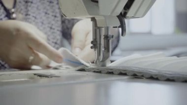 Atölyedeki bir terzi dikiş makinesine beyaz iplikçikli, hakiki deriden yapılmış bir ürün dikiyor.