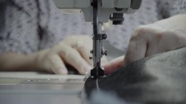 Atölyedeki bir terzi dikiş makinesine beyaz iplikçikli, hakiki deriden yapılmış bir ürün dikiyor.