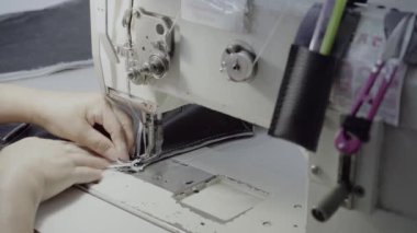 Atölyedeki bir terzi dikiş makinesine beyaz iplikçikli, hakiki deriden yapılmış bir ürün dikiyor.