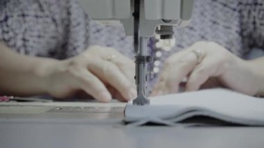 Atölyedeki bir terzi dikiş makinesine beyaz iplikçikli, hakiki deriden yapılmış bir ürün dikiyor.