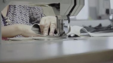 Atölyedeki bir terzi dikiş makinesine beyaz iplikçikli, hakiki deriden yapılmış bir ürün dikiyor.
