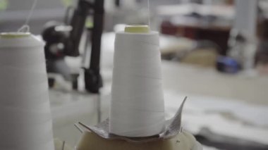 Dikiş makinesi atölyede çalışırken beyaz iplikler dönüyor.