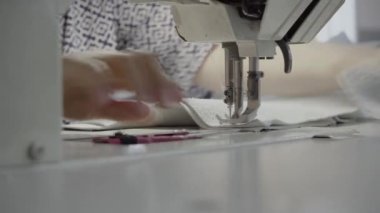 Atölyedeki bir terzi dikiş makinesine beyaz iplikçikli, hakiki deriden yapılmış bir ürün dikiyor.