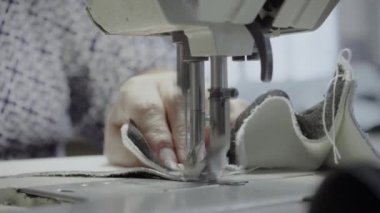 Atölyedeki bir terzi dikiş makinesine beyaz iplikçikli, hakiki deriden yapılmış bir ürün dikiyor.