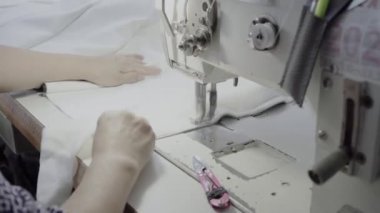 Atölyedeki bir terzi dikiş makinesine beyaz iplikçikli, hakiki deriden yapılmış bir ürün dikiyor.