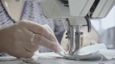 Atölyedeki bir terzi dikiş makinesine beyaz iplikçikli, hakiki deriden yapılmış bir ürün dikiyor.