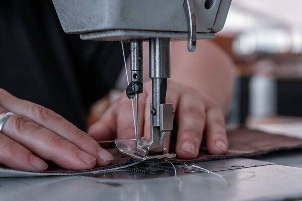 The seamstress sews at the sewing machine, threads the fabric. Women's hands