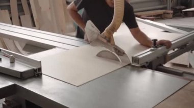 Bir fabrika işçisi dairesel testere ile bir ağaç keser. Kontrplak talaşı uçuyor.