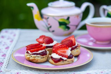 Freshly baked scones with tea served in the garden clipart