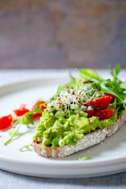 Avokado, domates ve yonca filizli çavdar tostu.