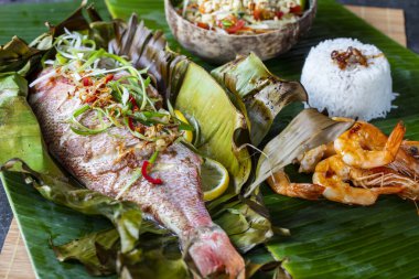 Muz yaprağında pişmiş kırmızı balık, papaya salatası ve pilav.