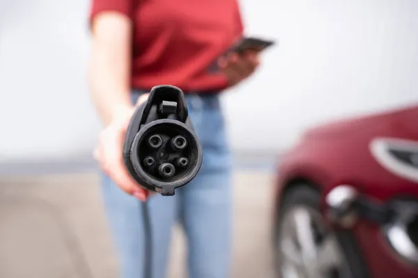 Vrouw met smartphone toont elektrische auto opladen plug — Stockfoto