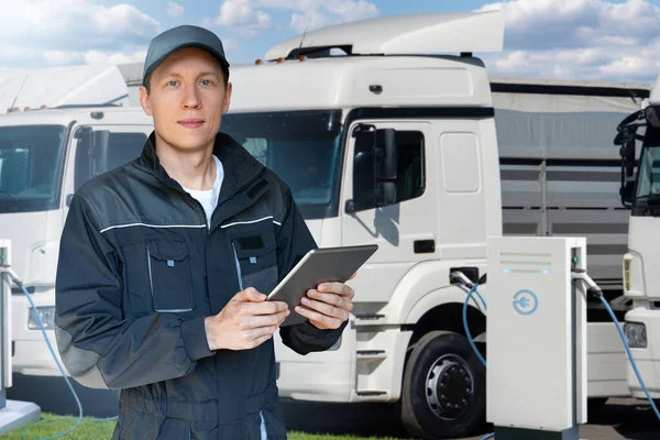 Fleet manager with a digital tablet stands next to electric trucks at electric vehicle charging stations