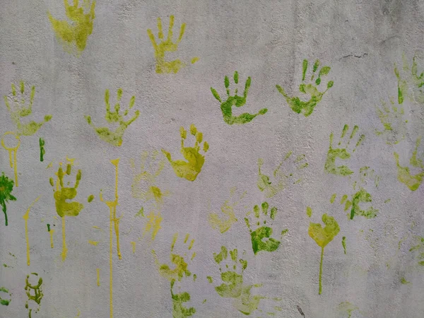 Green and yellow child\'s handprint on a white wall