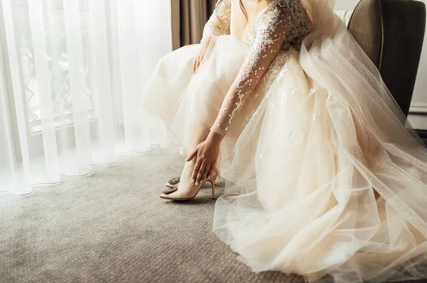 Mempelai wanita dengan gaun renda mengenakan sepatu pernikahannya dan meluruskan mereka dengan tangannya — Stok Foto