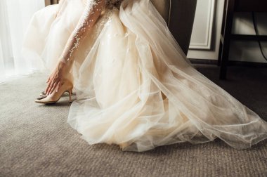 Dantel elbiseli gelin, düğün ayakkabılarını giyer ve elleriyle düzeltir.