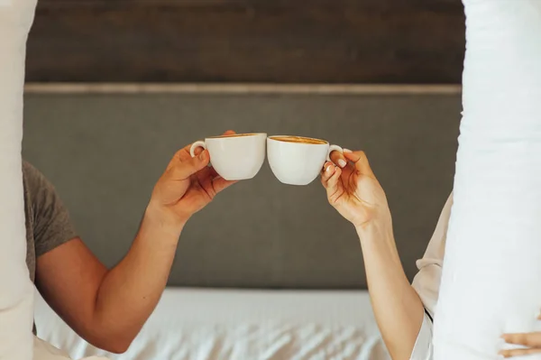 O pereche de mâini se țin deasupra păturii din pat țin cești de cafea. Dimineața — Fotografie, imagine de stoc