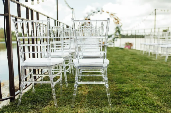 Arc rond pour une cérémonie de mariage près de la rivière. Chaises en verre blanc stand pour les invités — Photo