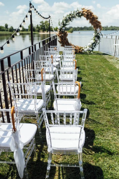 Kerek ív egy esküvői szertartáshoz a folyónál. Fehér üvegszékek állnak a vendégek rendelkezésére — Stock Fotó