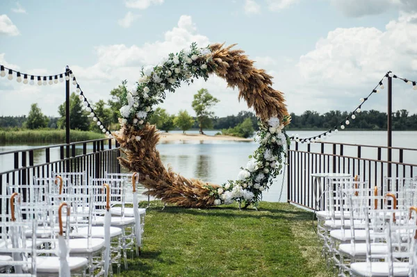 Arco redondo de uma cerimônia de casamento pelo rio. Cadeiras de vidro branco para os hóspedes — Fotografia de Stock