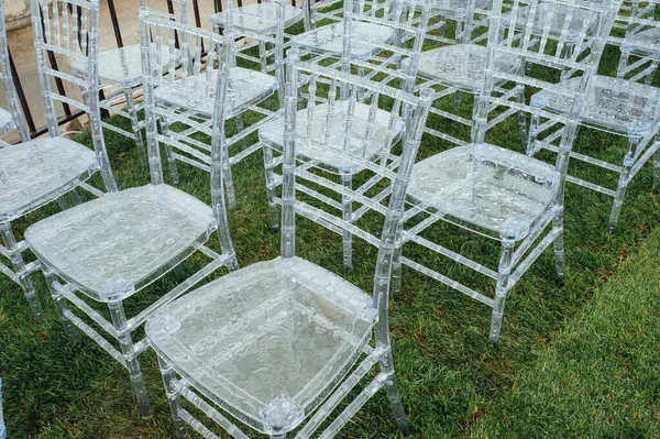 Des chaises en verre blanc se tiennent sur l'herbe verte. Arc rond pour une cérémonie de mariage en arrière-plan. Jour de pluie — Photo