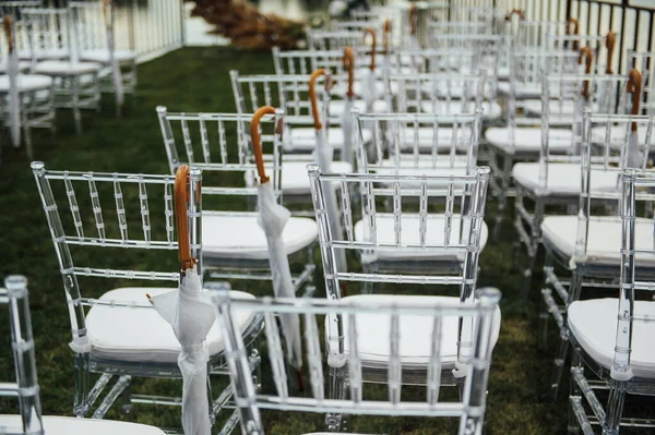 Bílá skleněná křesla stojí na zelené trávě. Kulatý oblouk pro svatební obřad v pozadí — Stock fotografie