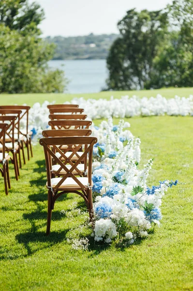 Cerimônia ao ar livre incrivelmente bonita na grama verde e cadeiras de madeira e flores frescas. Dia do casamento — Fotografia de Stock