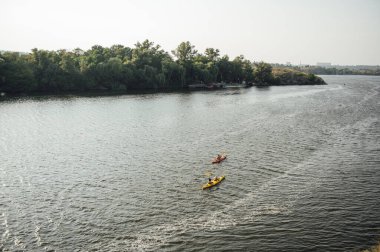 Yaz sabahı iki kadın ve bir erkek nehirde kayak yapıyor. Arka plan