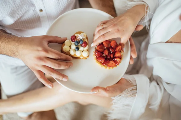 Happy couple having breakfast in bed with delicious cookies with strawberries on top — Foto de Stock