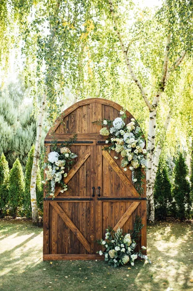 Ett vackert område för en utomhus bröllopsceremoni. Båge Dekorerad med en stor trädörr med många blommor. — Stockfoto