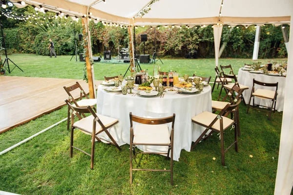 Ślub. Bankiet. Krzesła i okrągły stół dla gości, serwowane ze sztućcami. — Zdjęcie stockowe