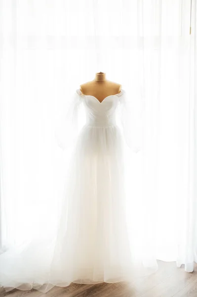 La robe de mariée est accrochée à la fenêtre. Un bouquet doux de la mariée et des chaussures pour femmes se tiennent sur le rebord de la fenêtre — Photo