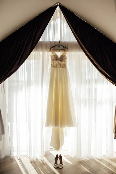 エレガントなウェディングドレスはカーテン付きの窓がかかっています。周辺には女性用の靴 — ストック写真