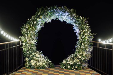 Taze çiçeklerle süslenmiş yuvarlak düğün kemeri. Akşam töreni.