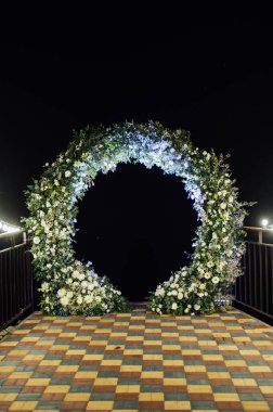 Taze çiçeklerle süslenmiş yuvarlak düğün kemeri. Akşam töreni.