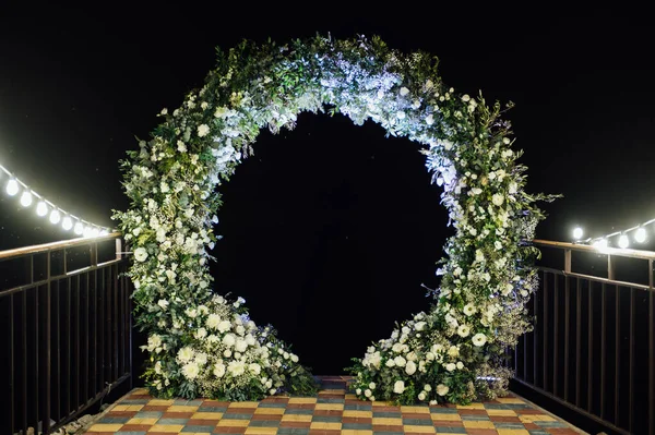 Taze çiçeklerle süslenmiş yuvarlak düğün kemeri. Akşam töreni.
