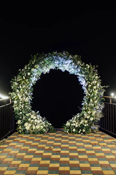 Taze çiçeklerle süslenmiş yuvarlak düğün kemeri. Akşam töreni.