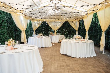 Bir düğün partisinin akşam dekorasyonu. Çiçekli ve lambalı konuklar için masalar.