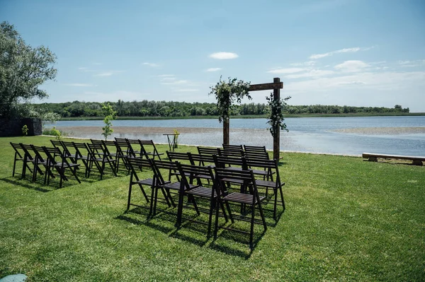 Wedding Arch and wooden chairs on the background beautiful river. Wedding wooden arch decorated with flowers.