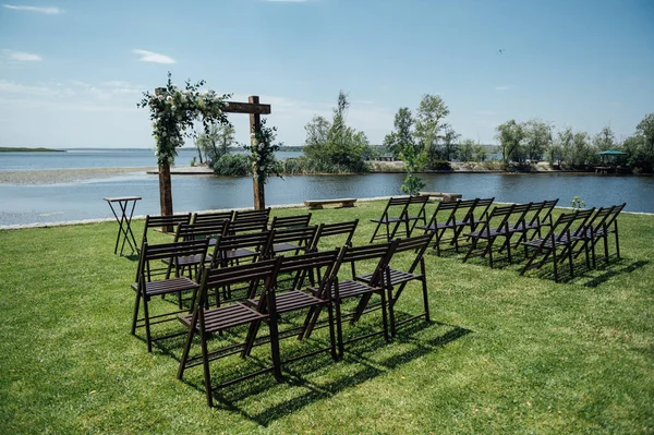 Wedding Arch and wooden chairs on the background beautiful river. Wedding wooden arch decorated with flowers.